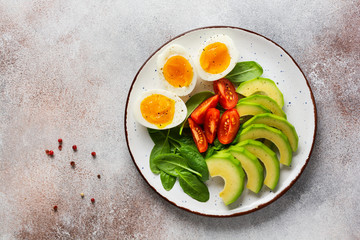 Healthy vegetarian salad breakfast. Spinach leaves, tomato, avocado and boiled egg on gray plate and gray concrete old background. Buddha bowl. Top view.