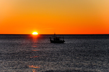 Obraz premium Dark silhouette of a fishing boat at sea during sunrise
