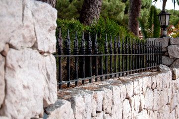 Stone fence with metal elements and a decorative lantern with background with green trees