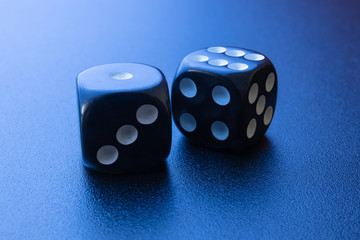Two black dice on a black matte background with side blue lighting. One and six.