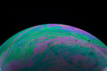 Soap bubble close up macro photography with colorful magenta, red, and green swirly pattern of...