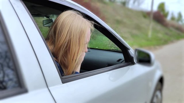 The blonde girl became ill from driving a car. Vomiting forced her to look out of the car so that the vomit would not enter the passenger compartment. The girl suffers from kinetosis, motion sickness.