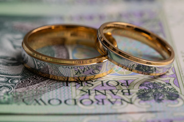 Gold wedding rings surrounded by a stack of Polish banknotes.