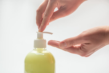 hands squeeze an antiseptic from a dispenser from a bottle with yellow liquid soap on a white background. Horizontal orientation.