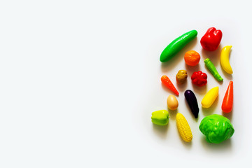 Still life with the image of colorful plastic children's fruit and vegetable toys on a white background. Top view with copy space.
