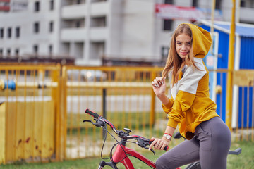 Fashion girl model in a yellow jacket posing in the city, sitting on a bicycle.