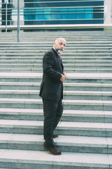 Full length portrait of confident businessman standing on stairs. Successful mature business consultant fastening button of suit. Concept of confidence