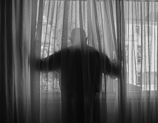 Hombre mira por la ventana de un edificio durante el confinamiento por el coronavirus COVID-19. La...