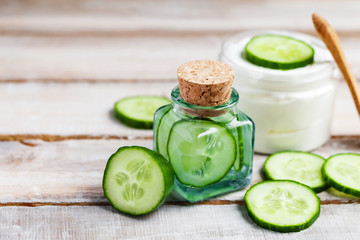 Concept of natural organic ingredients in cosmetology and home beauty treatment. Moisturizing gentle cream and mask for radiant shiny skin. Slices of fresh cucumber, wooden background, copy space