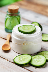 Concept of natural organic ingredients in cosmetology and home beauty treatment. Moisturizing gentle cream and mask for radiant shiny skin. Slices of fresh cucumber, wooden background, copy space
