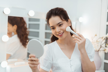 Beauty asian woman applying makeup. Beautiful girl looking on camera and applying cosmetic with a big brush on a cozy bedroom interior