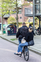 Two persons riding a bicycle on a city street of Amsterdam (the Netherlands)