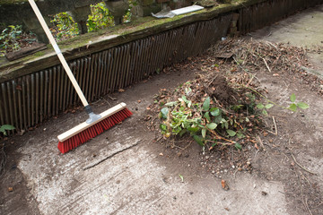 Garden broom brush with a pile of leaves in a garden yard.