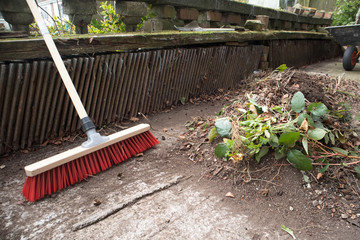 Garden broom brush with a pile of leaves in a garden yard.
