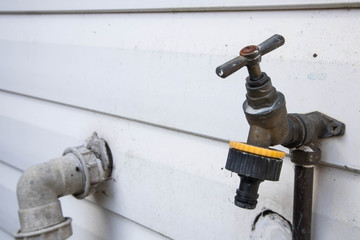 Old dirty brass external garden water tap on an exterior wall.