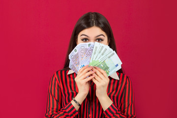 beautiful young woman with euro in hands on a red background	
