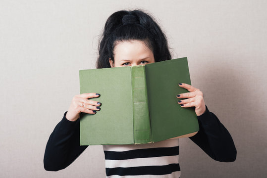 Woman looking from behind the book. On a gray background.