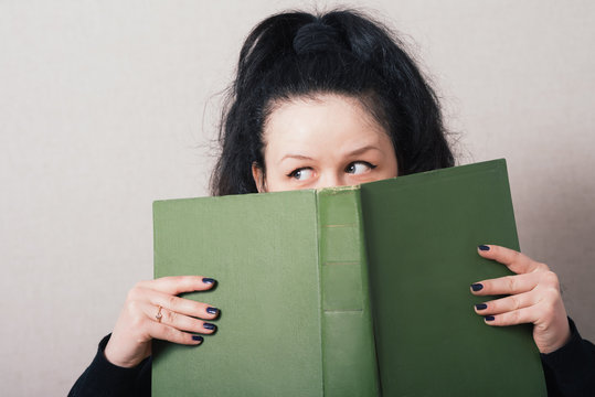 Woman looking from behind the book. On a gray background.
