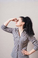 woman covering her eyes, hand covering her nose. On a gray background.