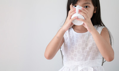 Asian girl in a white dress is drinking water or milk from a glass.