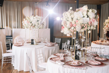 Wedding. Banquet. The chairs and round table for guests, served with cutlery, flowers and crockery and covered with a tablecloth with pink and white flowers and red plates