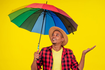 latin brazilian man with rainbow umbrella near color yellow wall