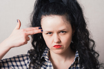 Obraz premium The woman making the gesture of suicide, the index finger to his temple, an imaginary gun. Gray background