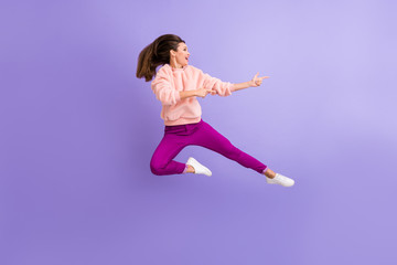 Fototapeta na wymiar Full length profile photo of cheerful lady jumping high indicating fingers empty space amazing sale wear casual fluffy pullover pants shoes isolated purple color background