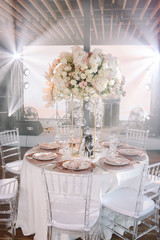 Wedding. Banquet. The chairs and round table for guests, served with cutlery, flowers and crockery and covered with a tablecloth with pink and white flowers and red plates