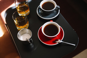 Top view on two cups of coffee, sugar and 2 glasses of whiskey on the black wooden table