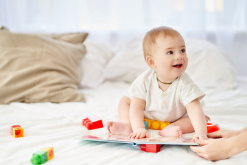 Obraz na płótnie Canvas Cute happy baby reading a children's book on a white soft bed