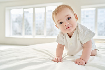 Close-up. A baby learns to crawl while standing on all fours on the bed.