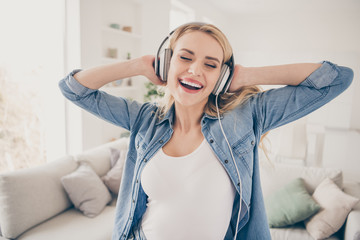 Naklejka premium Photo of pretty crazy blond lady rejoicing house party dancing near couch stay home listen cool earphones hold hands on ears eyes closed overjoyed quarantine time living room indoors