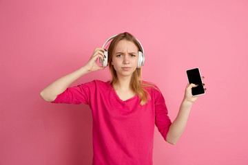 Naklejka premium Using gadget, devices. Caucasian young woman's portrait isolated on pink studio background, monochrome. Beautiful female model. Concept of human emotions, facial expression, sales, ad, trendy.