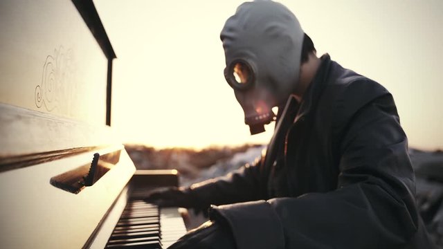 a girl in a black leather coat, in black gloves and a gas mask plays the piano among the ruins