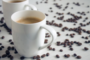 Two white coffee cups on a wooden table with copy space and scattered grains