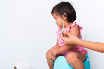 Asian little cute baby child girl training to sitting on blue chamber pot or potty her problem cannot shit and mother use Enema for help, studio shot isolated on white background, wc toilet concept