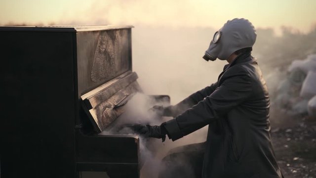 man in leather clothes and gas mask playing a smoking piano on the street