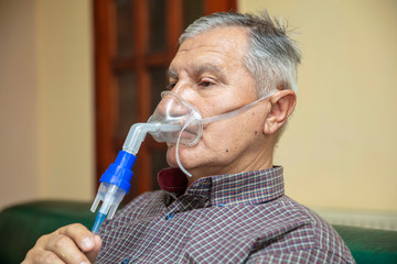 Senior man using medical equipment for inhalation with respiratory mask, nebulizer