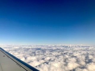 Fototapeta na wymiar High up in the stratosphere, close to heaven: Above the white clouds on a scenic journey in an airplane flight of a vacation journey seeing the aircraft wing gliding over the bright cloudscape