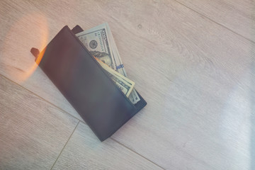 Black leather wallet with American dollars on a gray wooden floor. Close-up with sunflares. Finds money concept