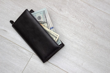 Black leather wallet with american dollars on a background of gray wood floor, close-up. Full of money. Wealth and prosperity concept