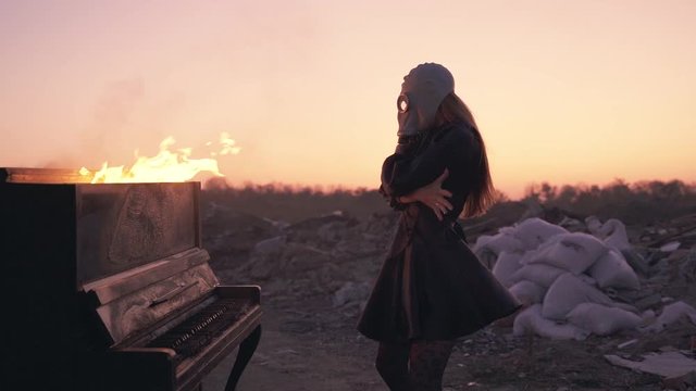 girl in a black dress and gas mask dancing near a burning piano