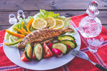 fried fish dish with vegetables and vodka on a tablecloth