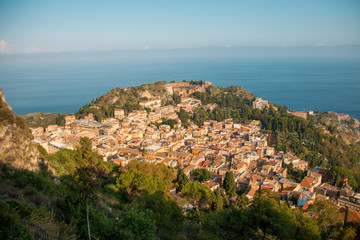 Fototapeta na wymiar Beautiful panorama from mountain top to a small mediterranean sicilian town, Taormina, in warm sunset with the sea in the background, Sicily, Italy 