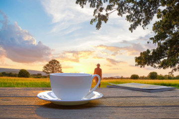 A cup of coffee on wooden table at natural green field in the morning sunrise.