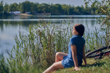 Lake with tall grass. Blurred silhouette of a resting girl with a bicycle. Weekend, outdoor recreation.