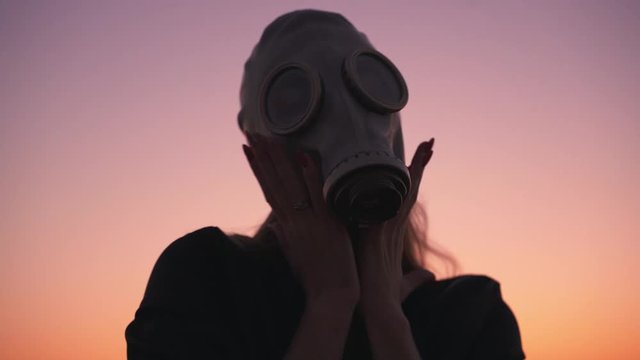 hands and face of a girl in a gas mask at sunset