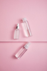 Top view of transparent cosmetic bottle, spray and serum bottle with liquid on pink paper background