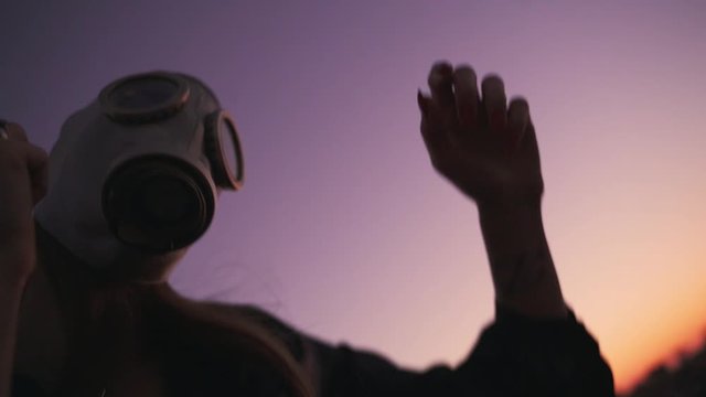 hands and face of a girl in a gas mask at sunset